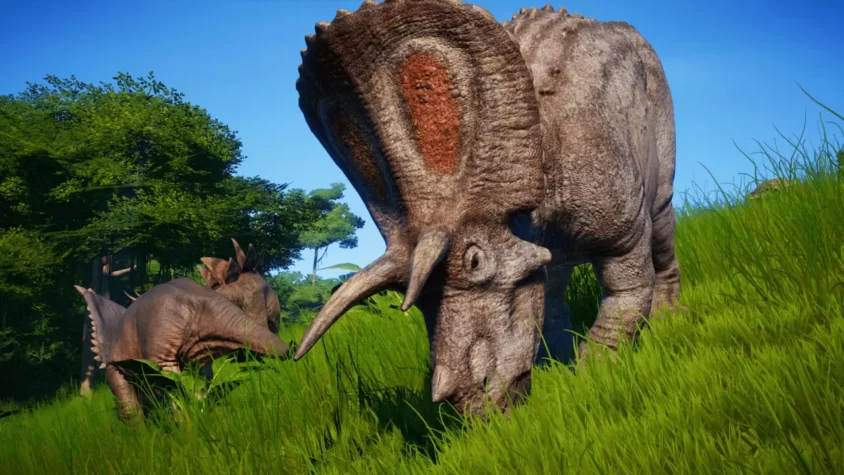 Трицератопс пасётся на зелёном лугу рядом с другим динозавром в Jurassic World Evolution