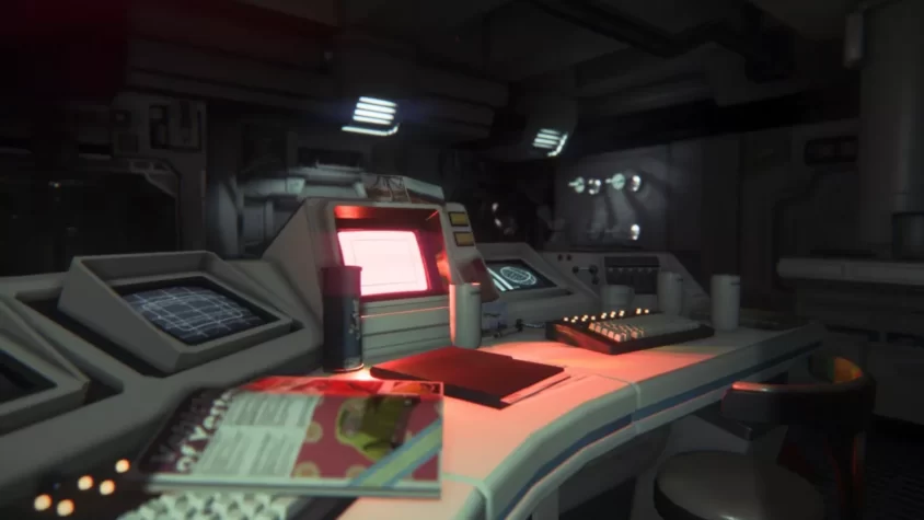 Кадр из игры Alien: Isolation с видом на рабочее место с компьютерами, документами и чашками