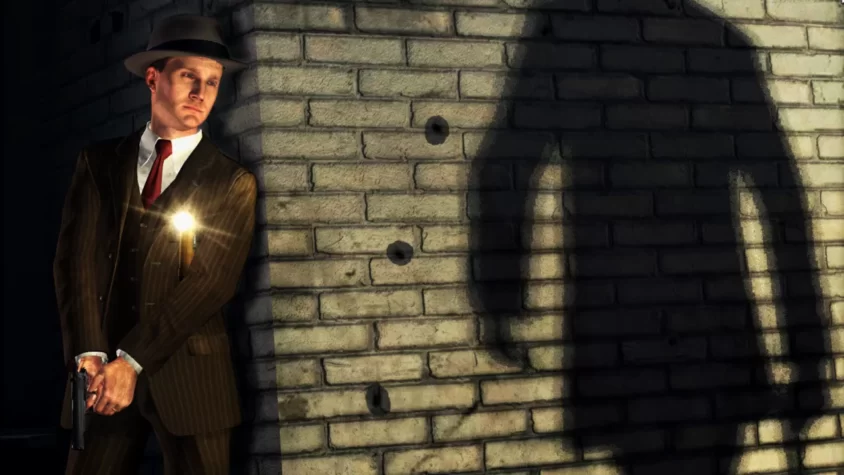 Герой L.A. Noire, стоящий в темном переулке, пока его тень угрожающе растет на кирпичной стене